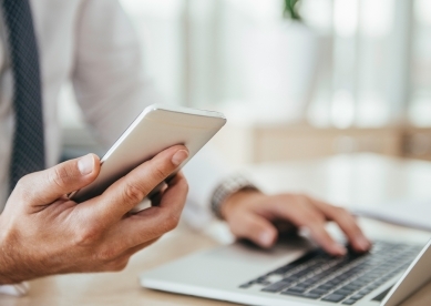 Midsection Of Businessman Using Laptop While Holding Mobile Phone On Table In Office